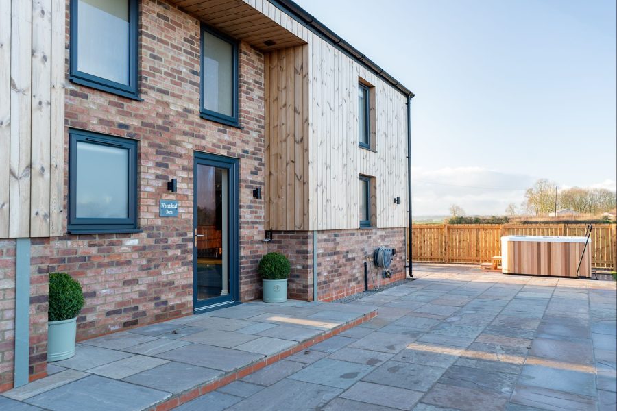 Exterior of Wheatsheaf Barn, a large self-catering holiday cottage with brick and timber cladding, private entrance, and paved walkway.