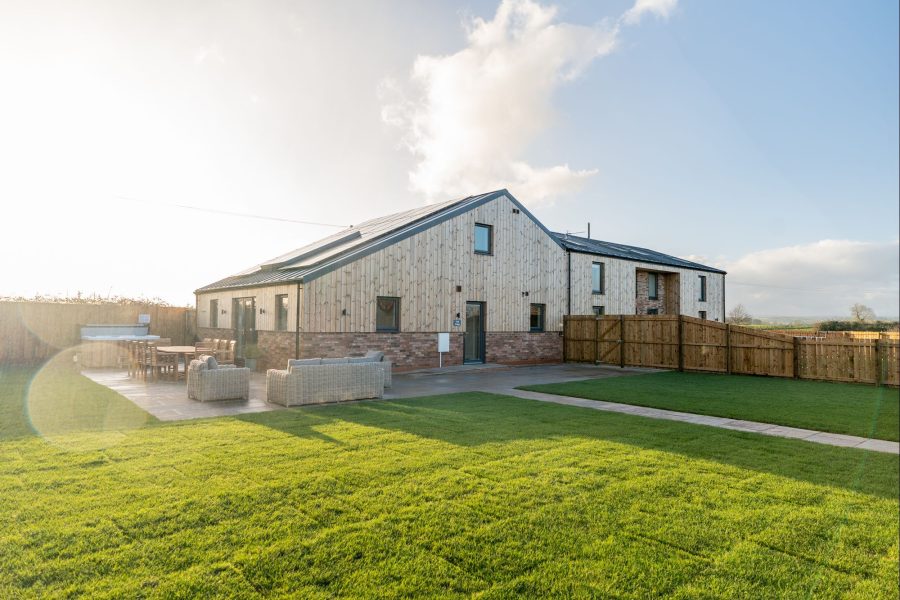 Exterior of Field Cottage, a large self-catering holiday cottage with brick and timber cladding, private entrance, lawn, outdoor seating, and paved walkway.