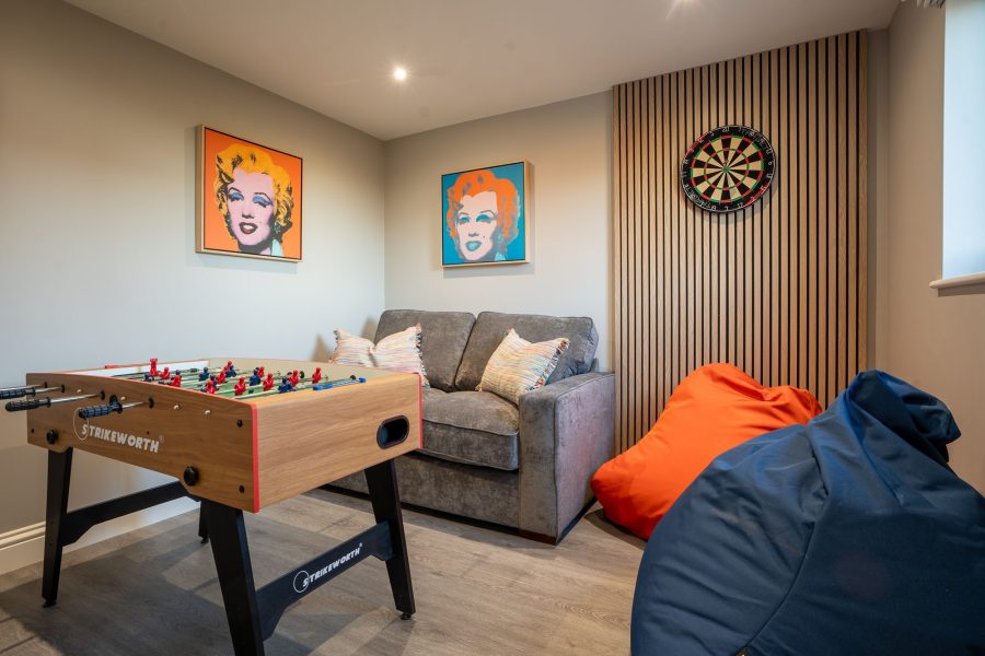Games room at Field Cottage, a large self-catering holiday cottage, with table football, dartboard, small sofa, beanbags, and framed pop-art prints.