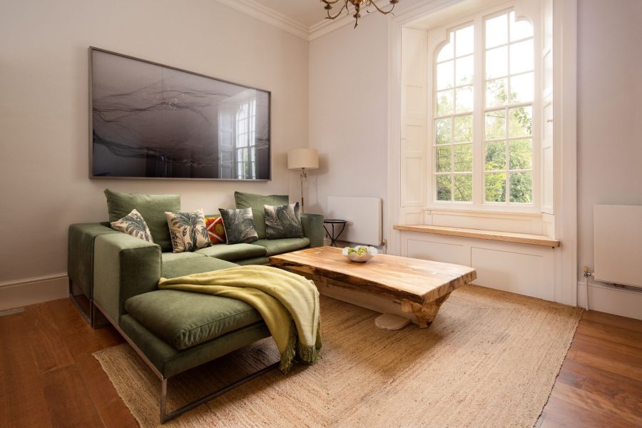 Living area at Aquarius Rising with a green corner sofa, wooden coffee table, and tall sash window.