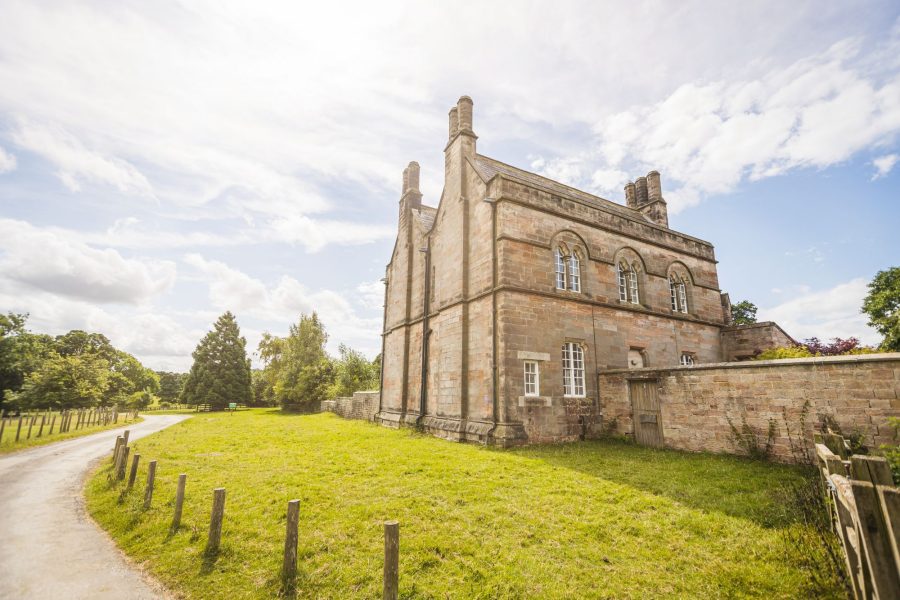 Exterior of Aquarius Rising, a historic stone building with arched windows and tall chimneys set beside open countryside.