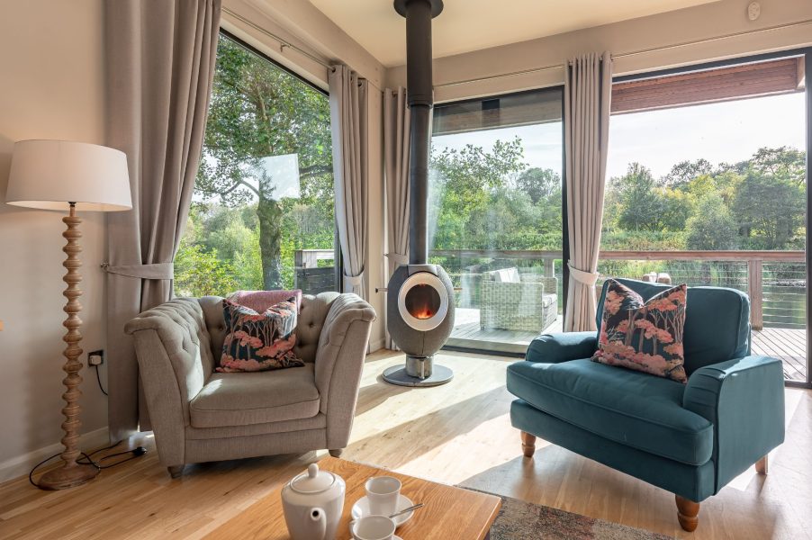Open-plan living area with wood burner, sofa seating and lake views in Finley lodge, Brompton Lakes. 