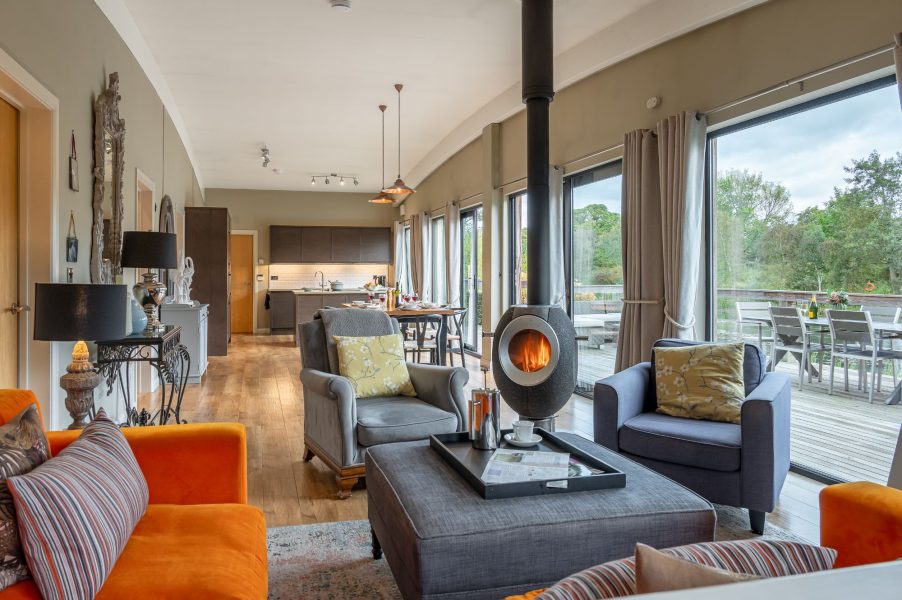 Open-plan living area with living area, dining table, kitchen and access to lakeside decking in Juniper lodge, Brompton Lakes.