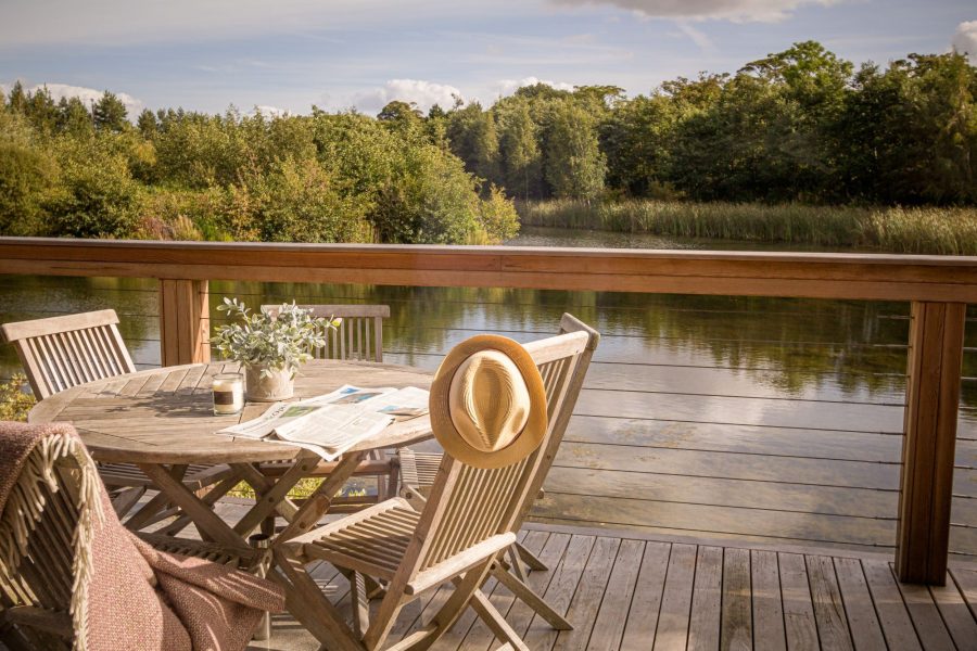 Private lakeside decking at William lodge at Brompton Lakes with outdoor dining table, chairs and peaceful water views.