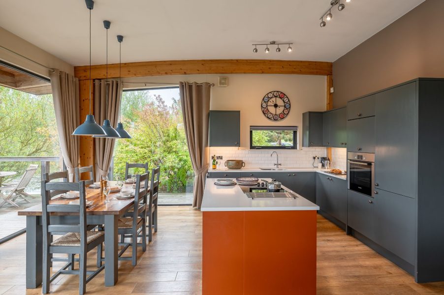 Open-plan kitchen and dining area in William lodge at Brompton Lakes with island, large windows and garden views.