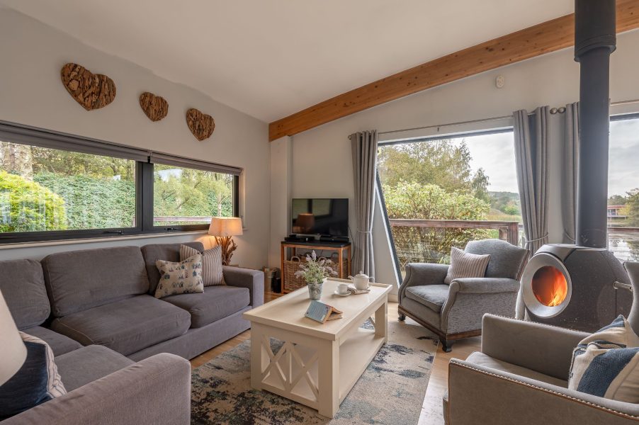 Cosy living area with log burner with large windows, sofas and armchairs in Iris lodge, Brompton Lakes.