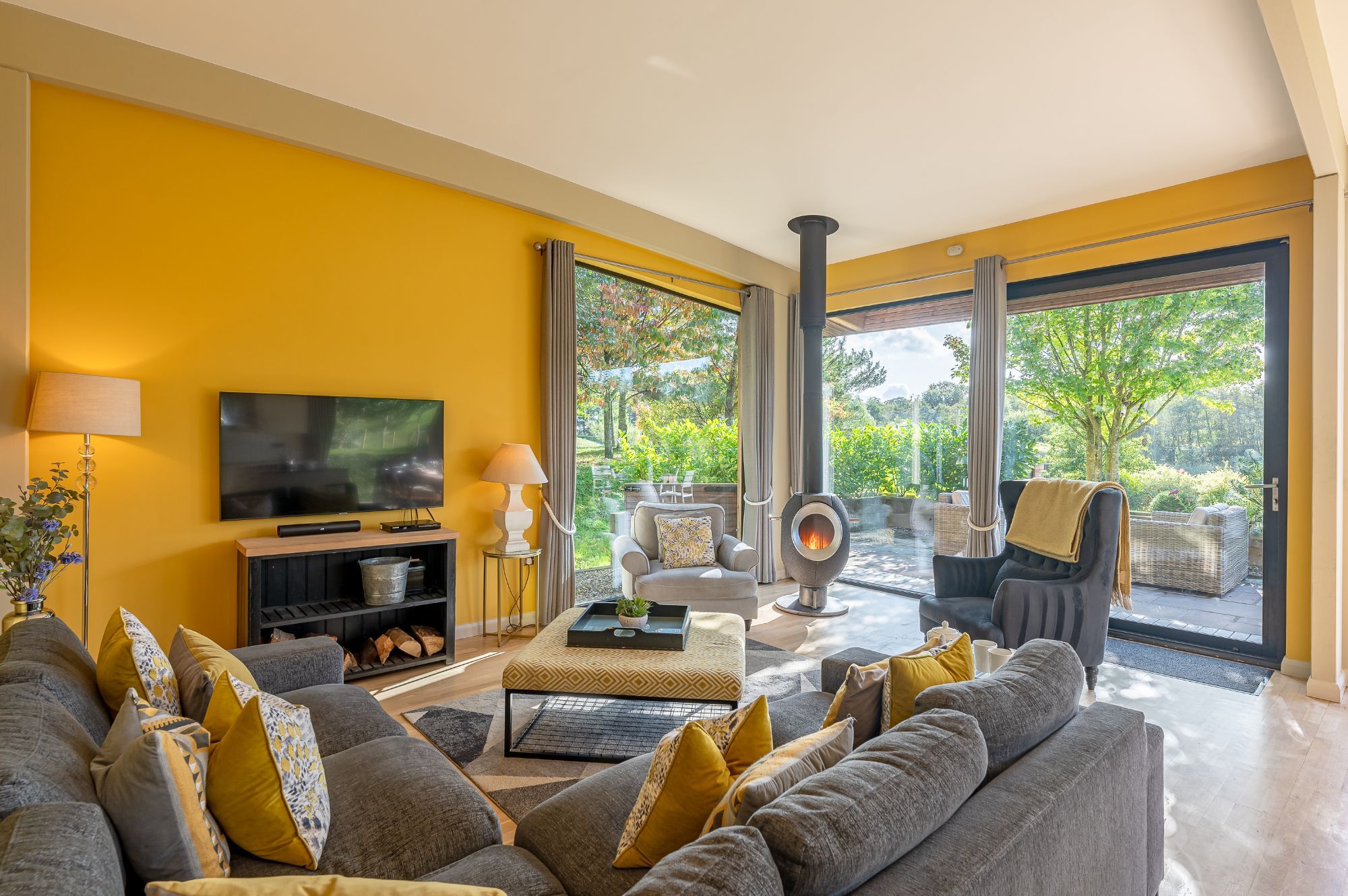 Open-plan living room with log burner and garden views at Percy lodge, Brompton Lakes.