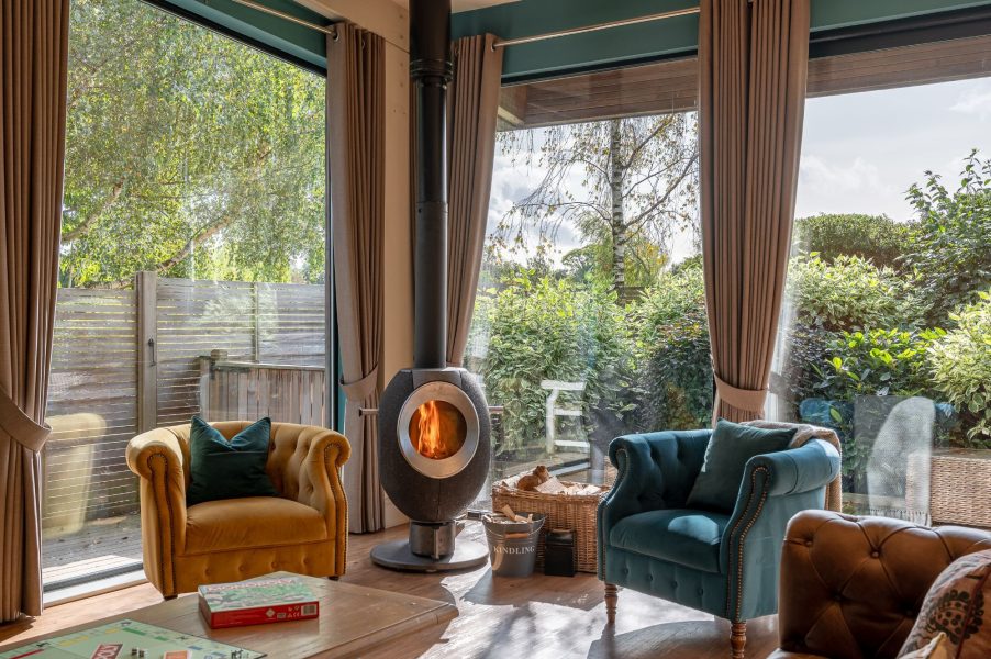 Cosy lounge with log burner and armchairs overlooking garden at Twenty One lodge at Brompton Lakes, North Yorkshire.