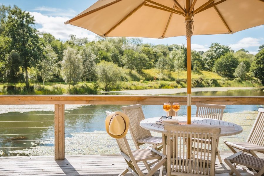 Private deck at Louis lodge with outdoor dining table, parasol and countryside views at Brompton Lakes.