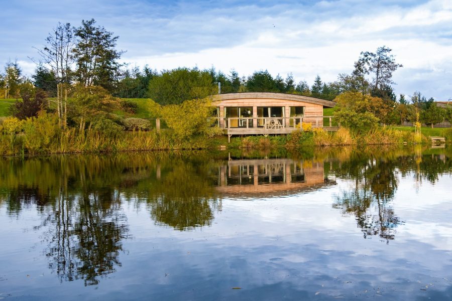 Exterior of Louis Lodge at Brompton Lakes reflected on tranquil lake in North Yorkshire.