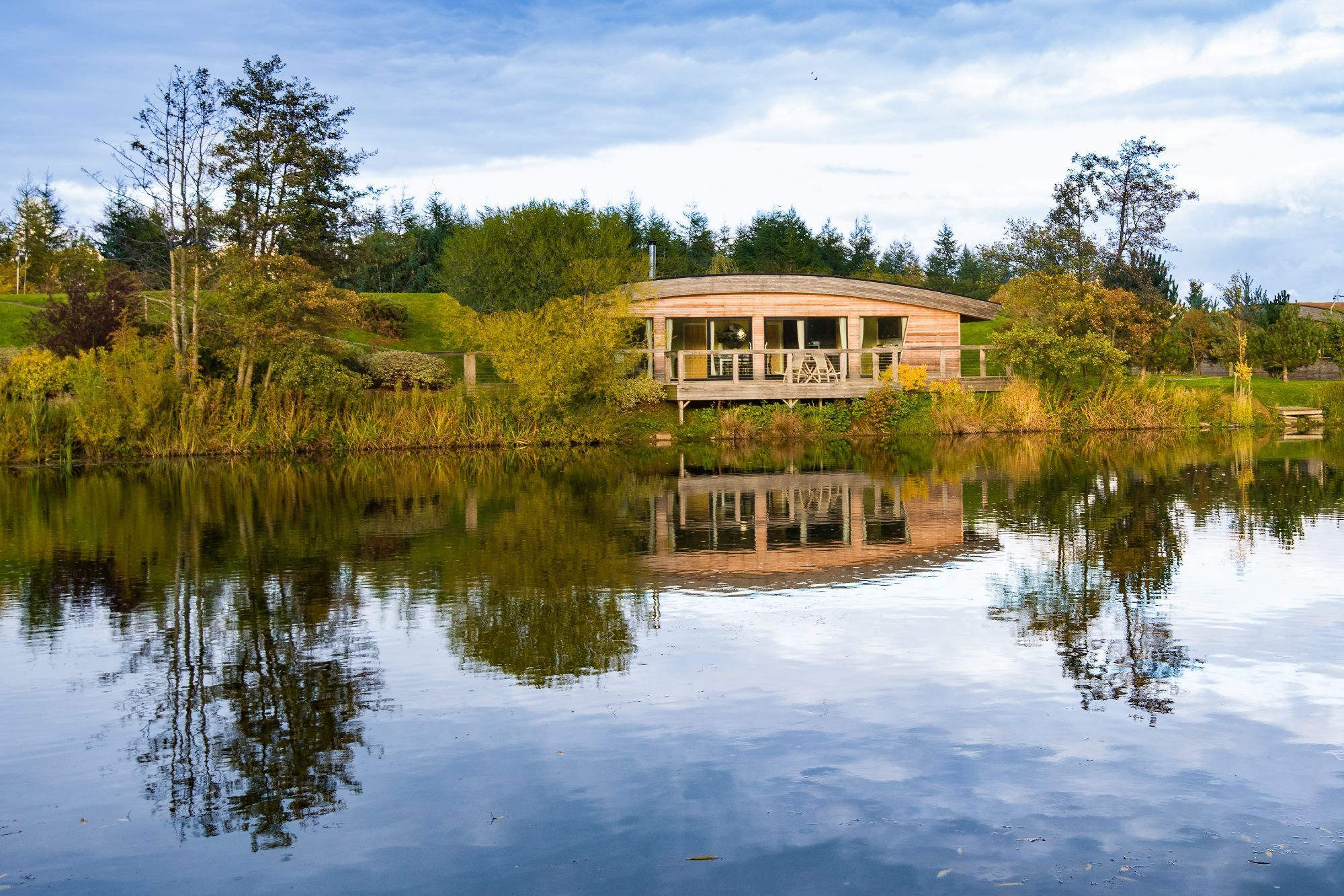 Exterior of Louis Lodge at Brompton Lakes reflected on tranquil lake in North Yorkshire.
