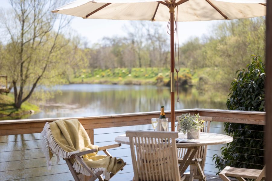 Private lakeside deck at Abbey, with outdoor wooden seating and dining beneath a parasol overlooking the water.