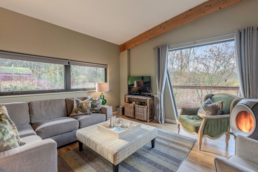 Comfortable living room in Rebecca lodge at Brompton Lakes with cosy sofa, log burner, large windows and stylish interiors.