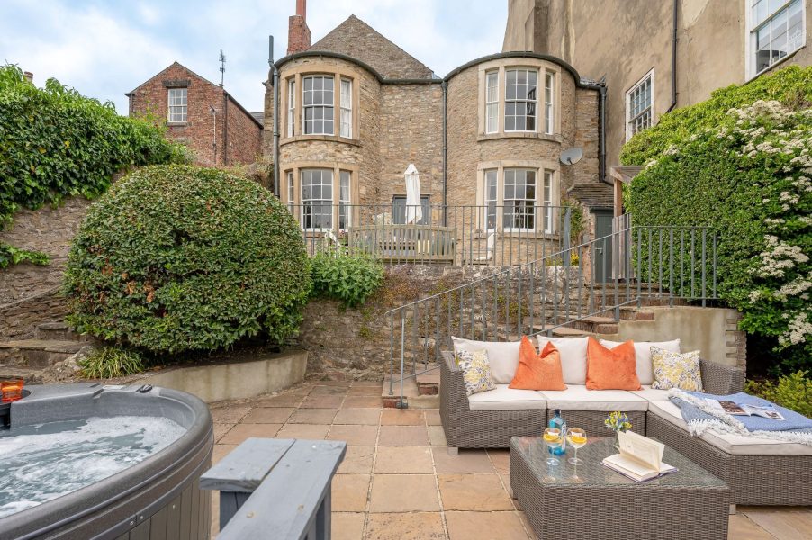 Courtyard patio at 30 Frenchgate with a hot tub, outdoor sofa seating, and a stone building with bay windows and steps up to a terrace.