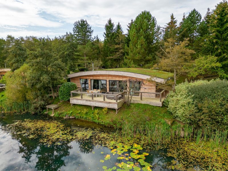 Exterior view of Abbey, a lakeside lodge with a large private deck overlooking the water and surrounding woodland.