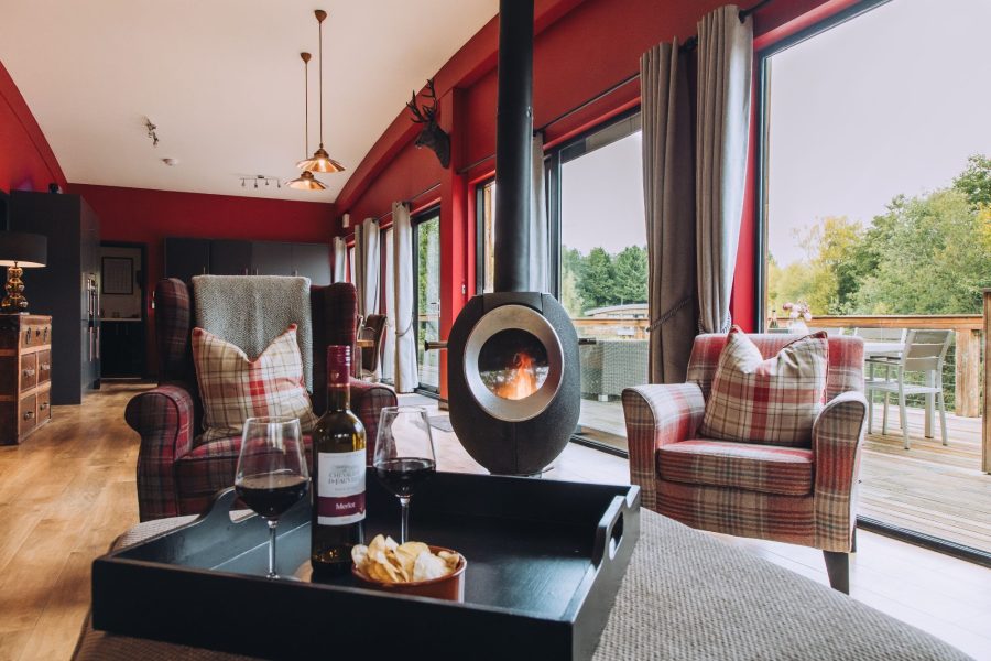 Seating area at Isabella with armchairs, a coffee table with drinks, a wood-burning stove, and large doors opening onto the deck
