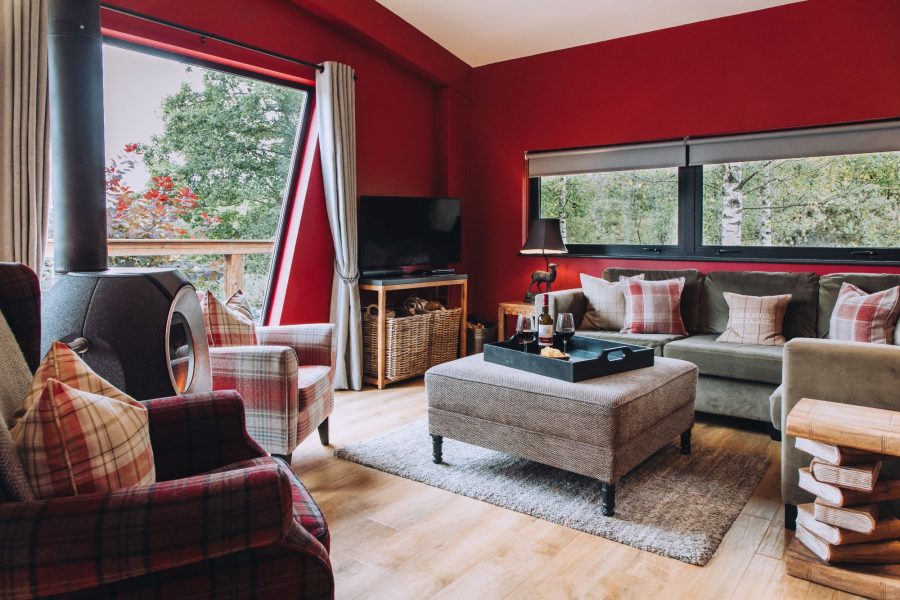 Living area at Isabella with a sofa, armchairs, coffee table with drinks, TV, wood-burning stove, and windows looking out to the trees.
