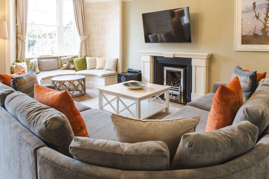 Living room at 30 Frenchgate with a curved sofa, coffee table, fireplace with wall-mounted TV above, and bay window seating area.