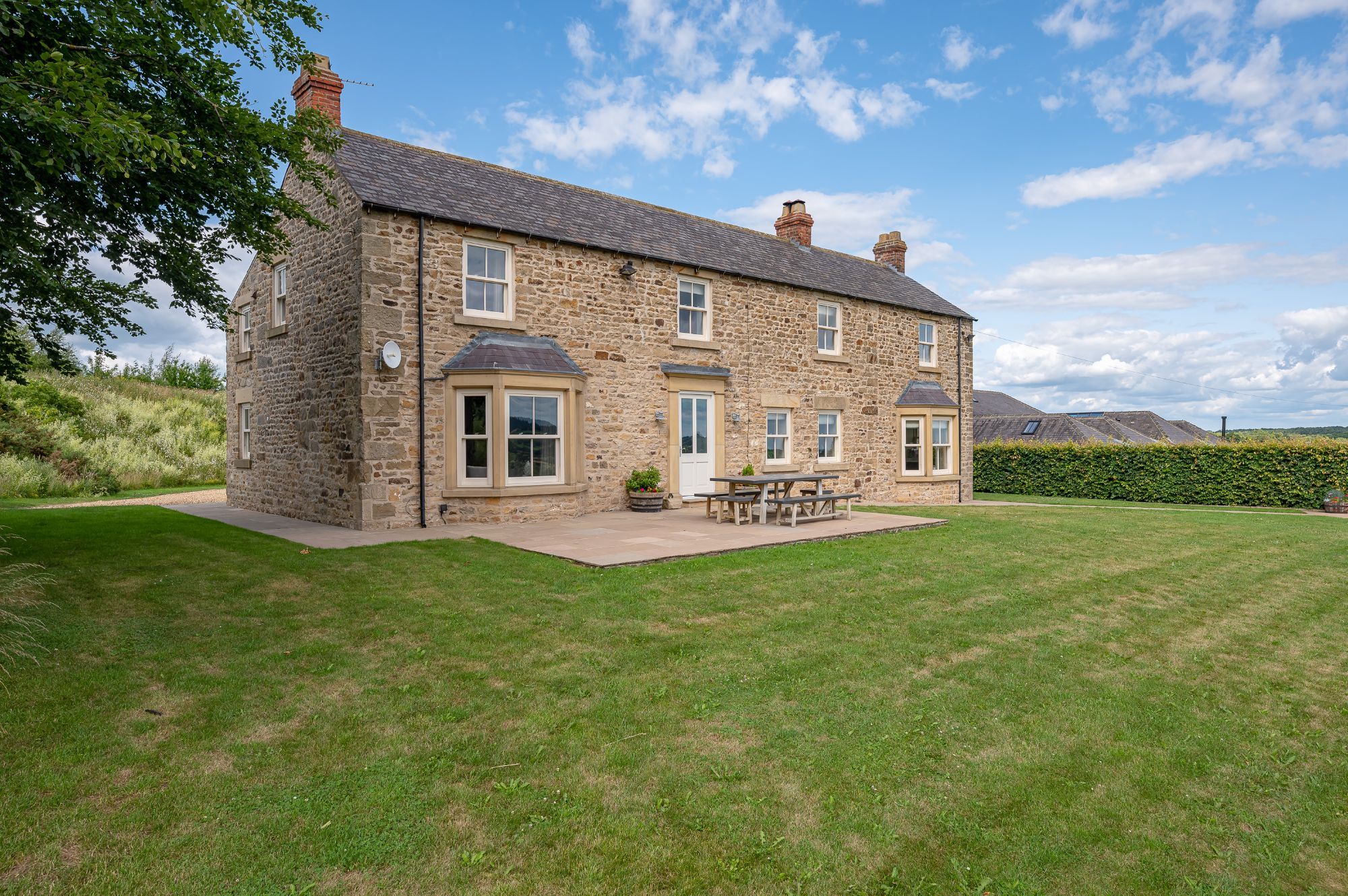 Exterior of The Farmhouse at Greenbank Barns with traditional stonework and large garden and outdoor seating area.