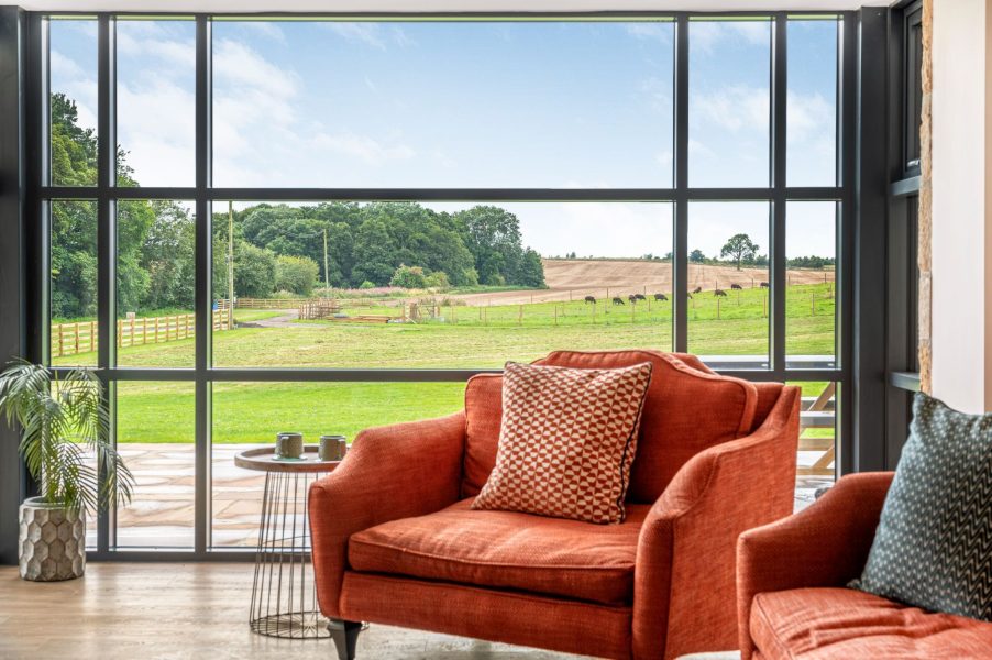 Stylish lounge with armchairs overlooking rural views through floor-to-ceiling windows in Dragonfly.