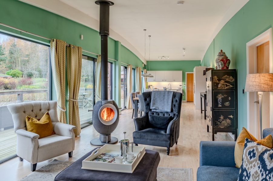 Open-plan living space in Coco lodge at Brompton Lakes with wood-burning stove, designer furnishings and lakeside views.