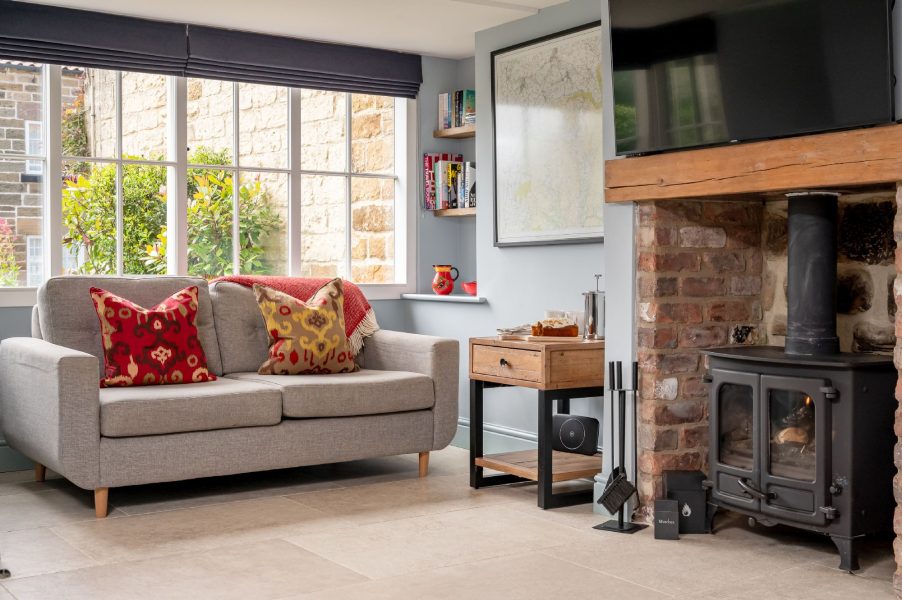 Cosy living area in Paddock View, Osmotherley with two-seater sofa, wood-burning stove, brick fireplace and large window views.