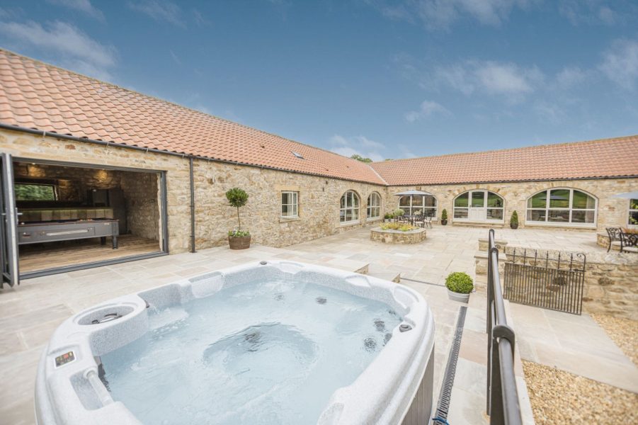 Luxury hot tub in private courtyard at Kingfisher cottage with surrounding stone buildings.