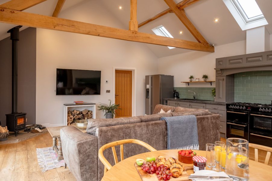 Open-plan kitchen and dining area with wooden beams and log burner in Millfield Barn.
