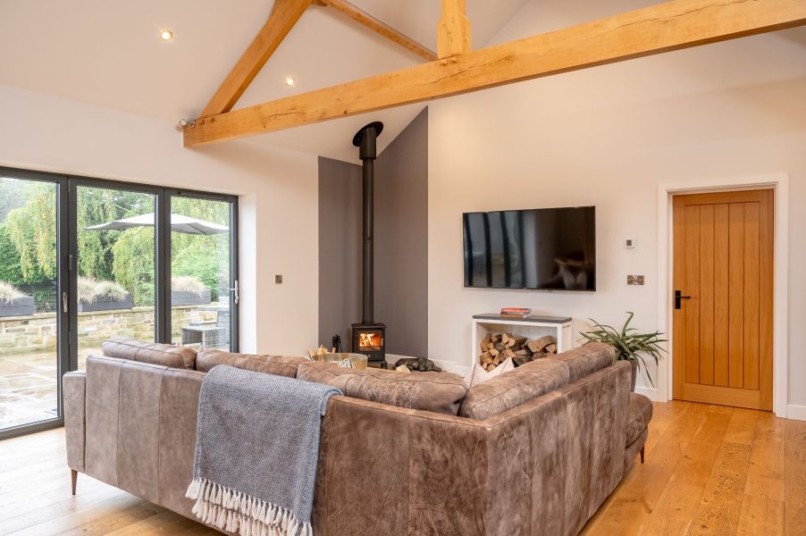 Cosy lounge with log burner, smart TV, comfortable seating and wooden beams in Millfield Barn.