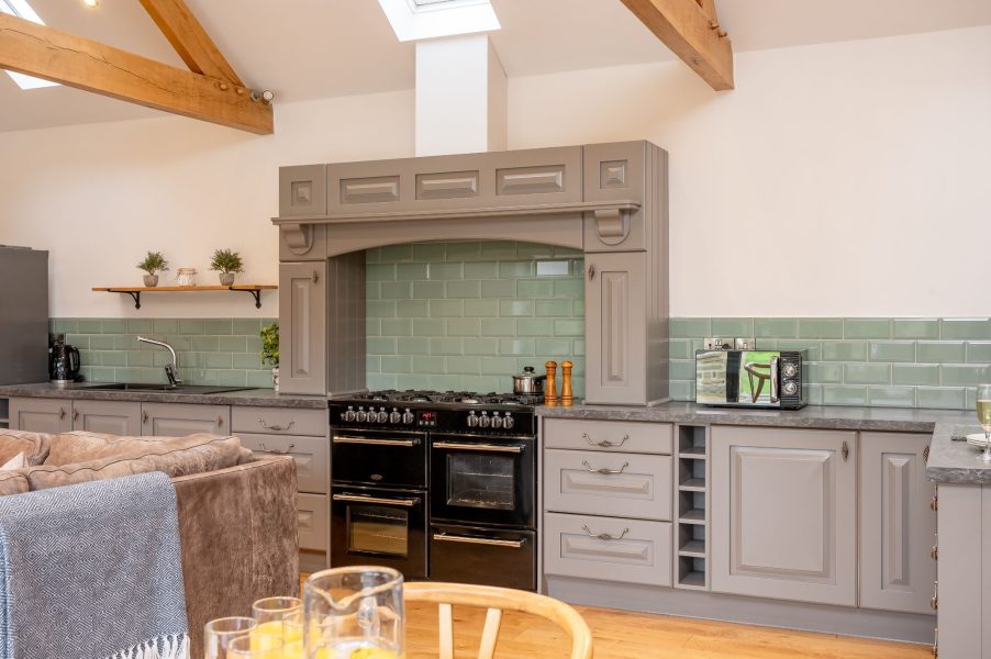 Open-plan kitchen with modern units and wooden beams in Millfield Barn.
