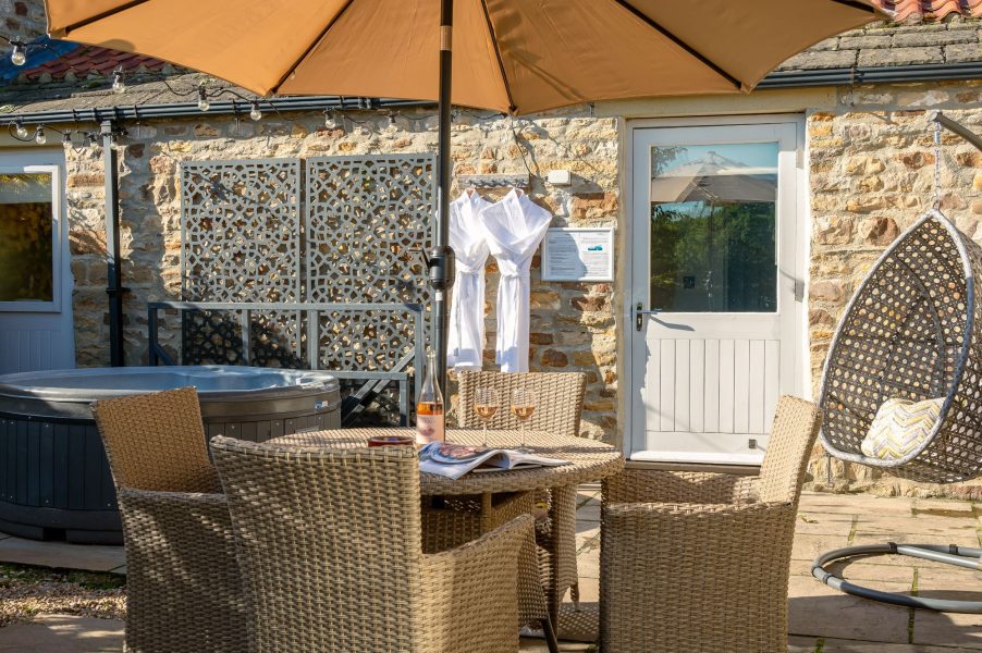 Spacious outdoor terrace with hot tub, dining table, parasol and stone cottage exterior in Austin cottage.