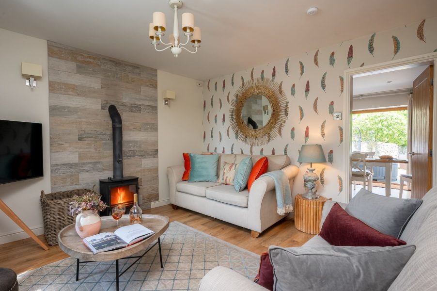 Comfortable lounge area in Woodcroft Cottage featuring log burner, soft furnishings, coffee table and modern rustic styling.