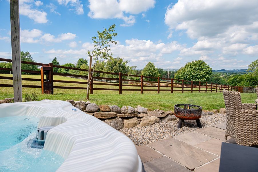 Outdoor hot tub at Constable Burton lodge with patio seating and fire pit.