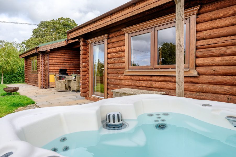 Outdoor hot tub at Hunters Lodge with patio seating and log cabin exterior.