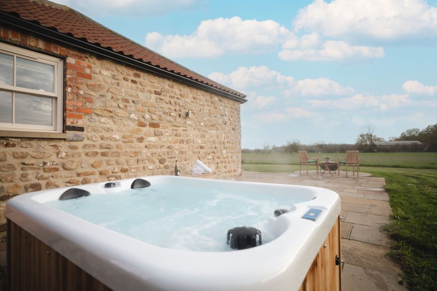 Private outdoor hot tub at Whitwell Nook holiday cottage in North Yorkshire with patio seating and rural setting.
