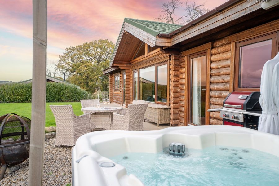 Exterior of Penhill lodge, a wooden log cabin with patio, hot tub and countryside views.
