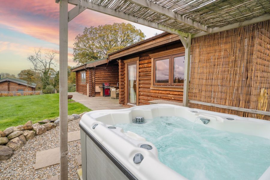 Outdoor hot tub at Rosina lodge with patio seating and traditonal log cabin exterior.