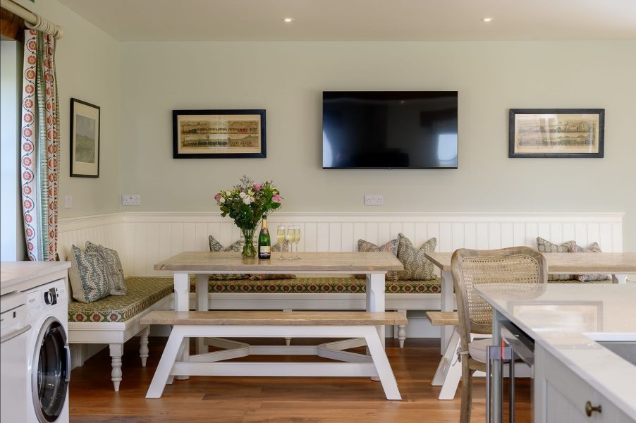 Dining area in Hollins Barn with bench seating, wooden table and wall-mounted TV.