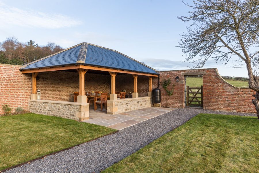 Outdoor covered dining area at Hollins Farmhouse with garden views and seating.