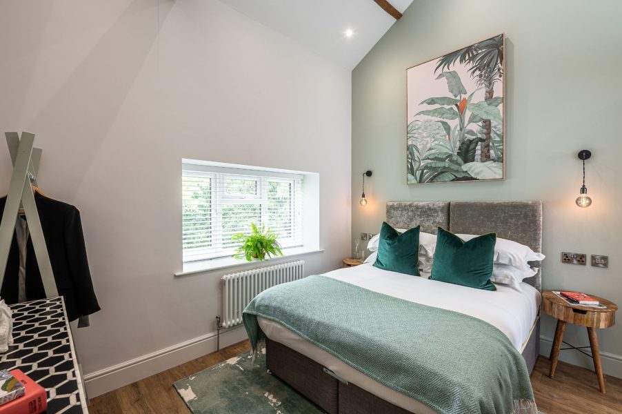 Stylish bedroom with green accent wall, double bed and botanical artwork in The Old Tack Room.