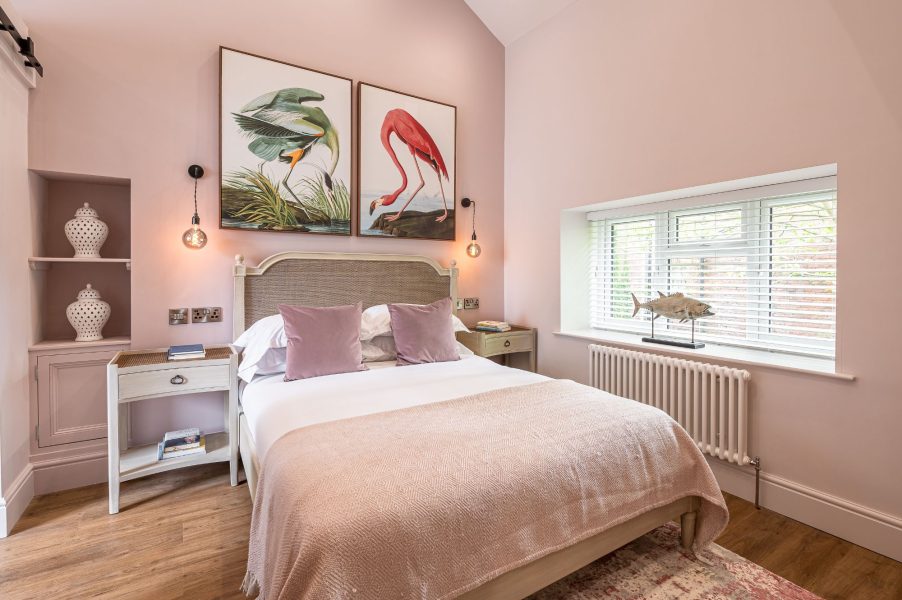 Elegant pink bedroom with double bed and framed bird prints in The Old Tack Room.