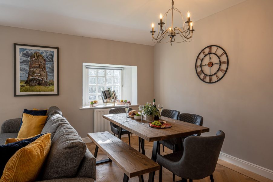 Stylish dining area in The Old Potting Shed with wooden table, upholstered chairs, and natural light from a window overlooking the countryside.