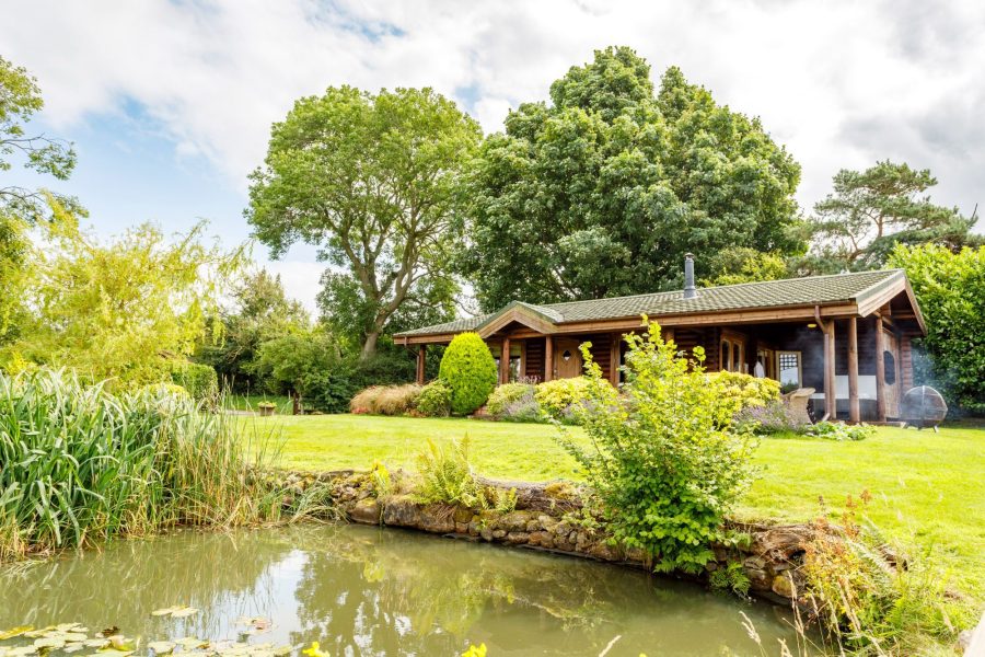 Exterior of Spindrifter log cabin, set in landscaped garden with pond and trees.