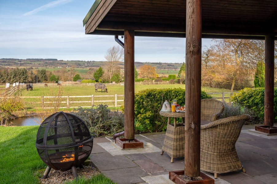 Covered patio with outdoor seating, fire pit and countryside views at Spindrifter luxury log cabin.