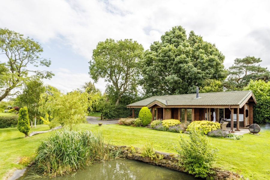 Exterior of Spindrifter log cabin, set in landscaped garden with pond and trees.