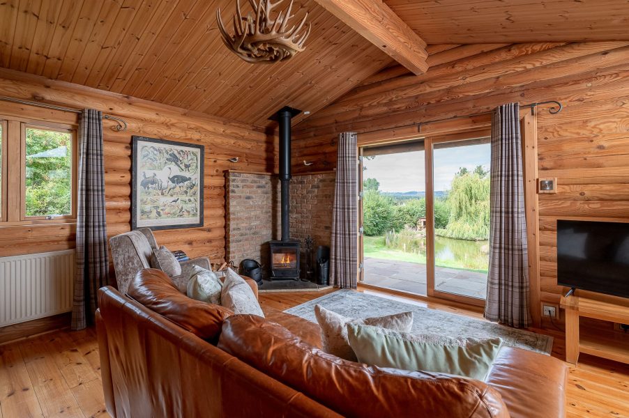 Lillie lodge living room with leather sofa, wood-burning stove, TV and patio doors to garden.