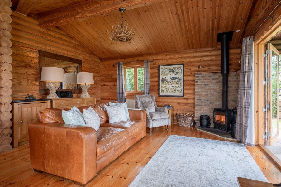 Lillie lodge living room with leather sofa, wood-burning stove and patio doors to garden.
