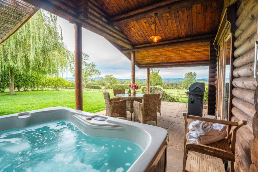 Outdoor hot tub, BBQ, and dining area with countryside views at Pivotal lodge.