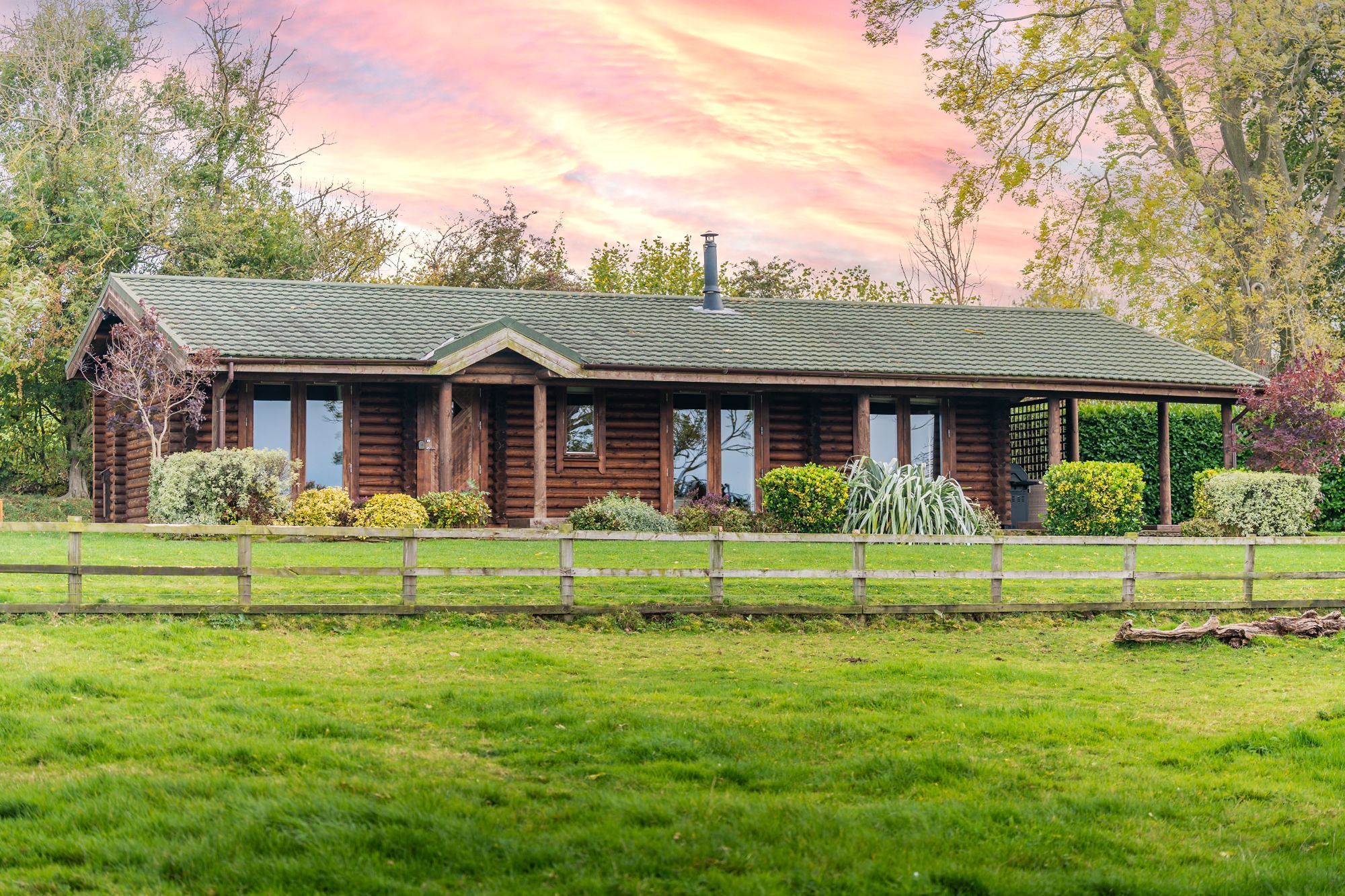 Exterior view of Alborada luxury log cabin with large private lawn and countryside surroundings.
