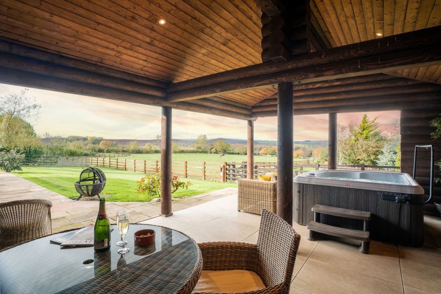 Covered outdoor terrace at Melody lodge with hot tub, dining table, barbecue and rustic wooden beams.